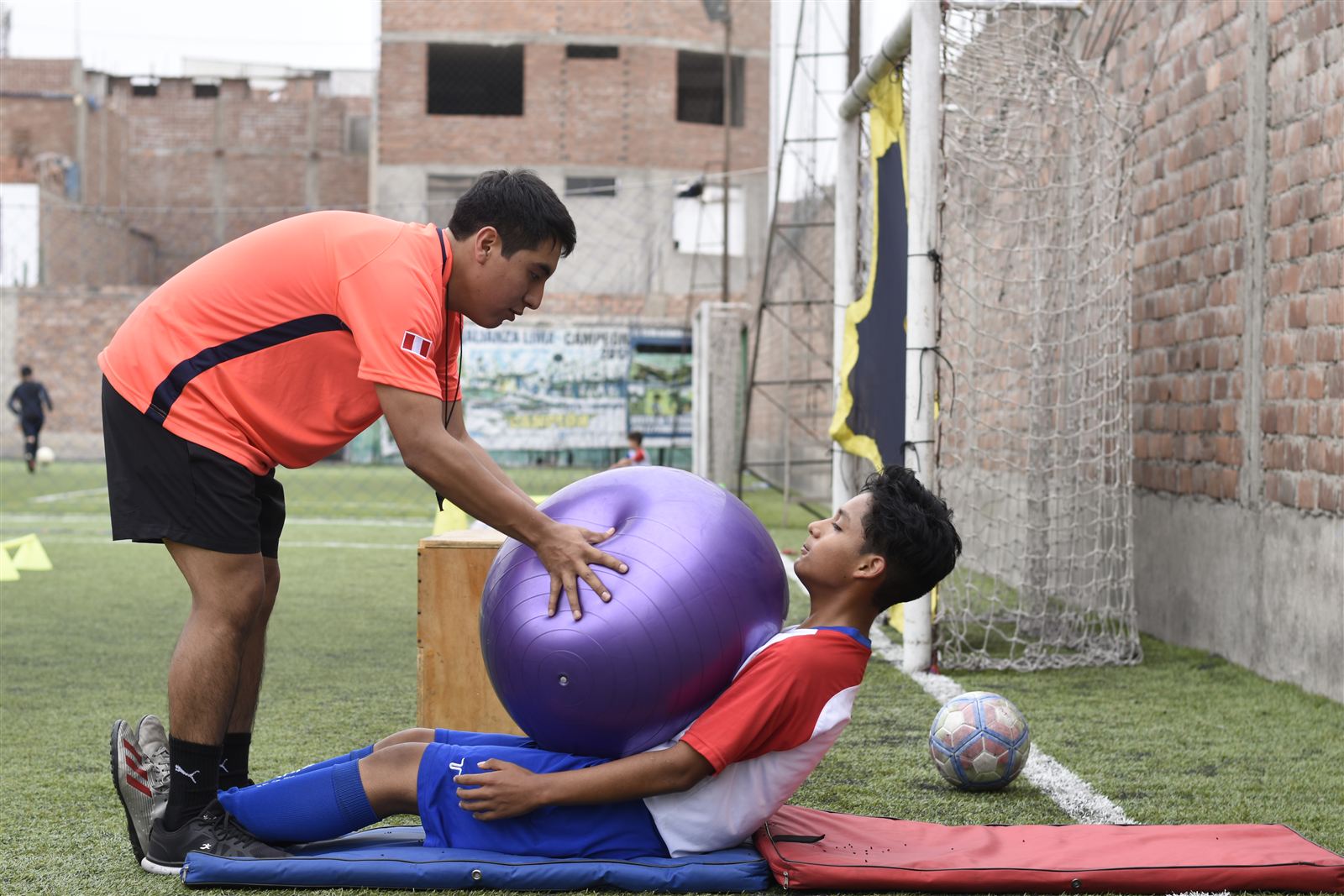 Entrenador guiando a un alumno en un ejercicio con balón suizo