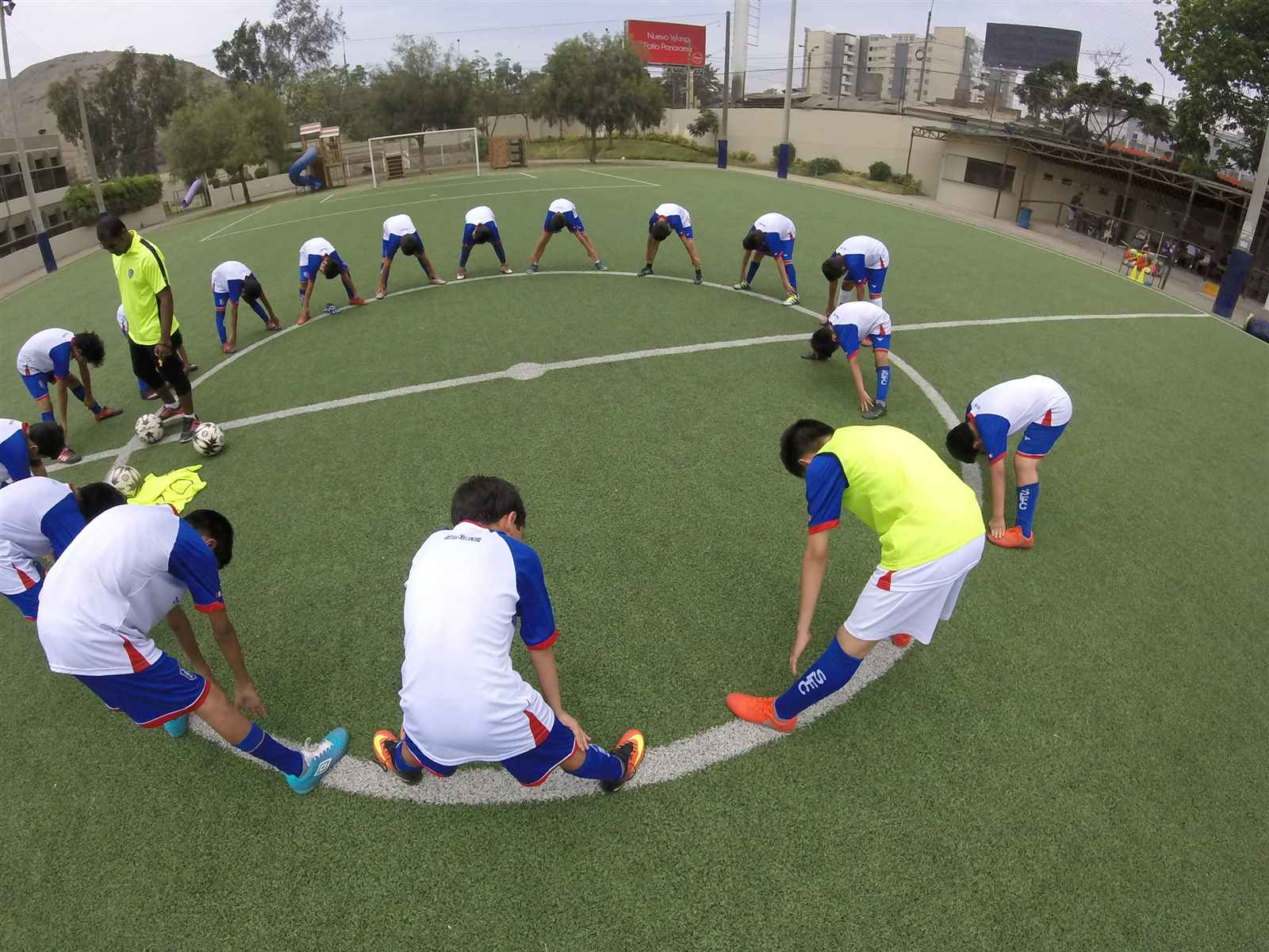 Alumnos de Soccer Lima FC en un círculo de estiramiento en la cancha, vistos desde arriba