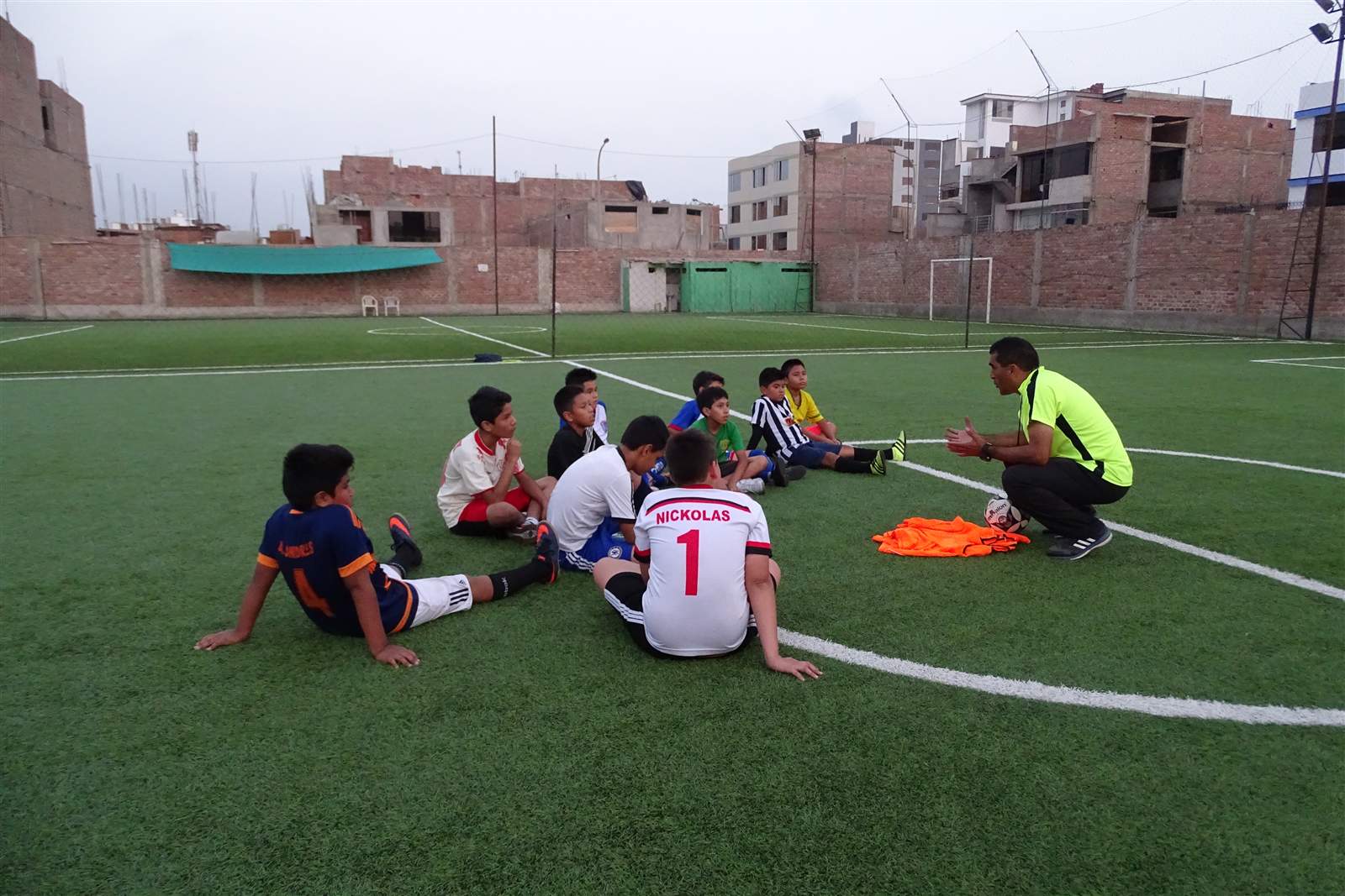 Alumnos sentados en círculo escuchando al entrenador en la cancha de Soccer Lima FC