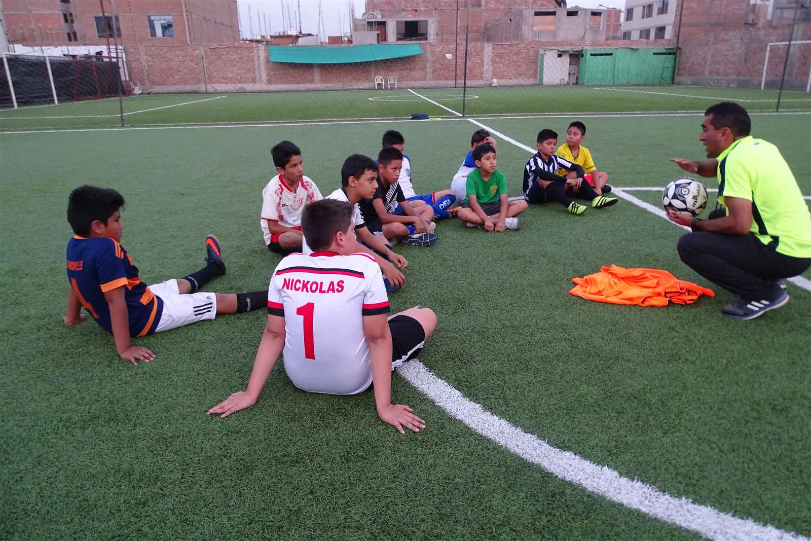 Alumnos sentados en círculo escuchando al entrenador en la cancha de Soccer Lima FC