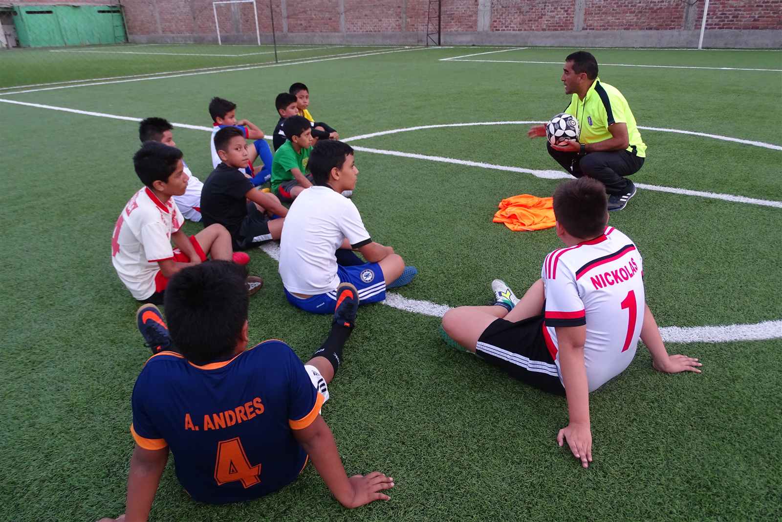 Alumnos sentados en círculo escuchando al entrenador en la cancha de Soccer Lima FC