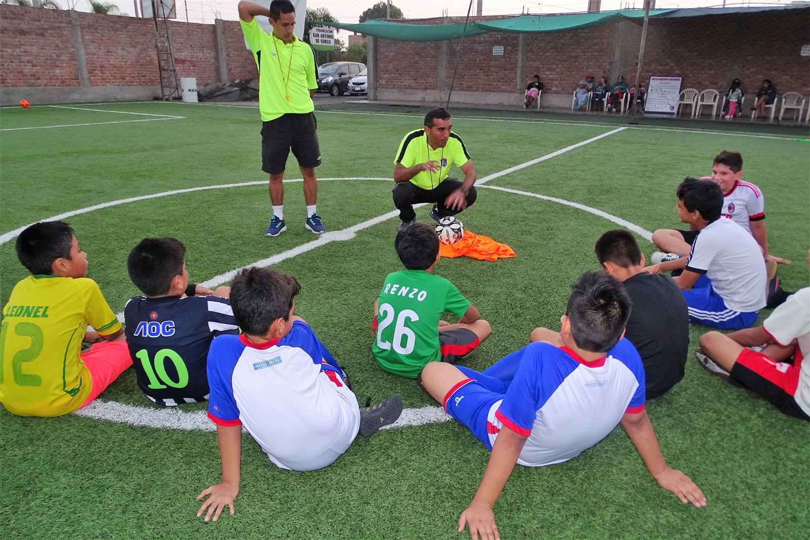 Alumnos sentados en círculo escuchando al entrenador en la cancha de Soccer Lima FC
