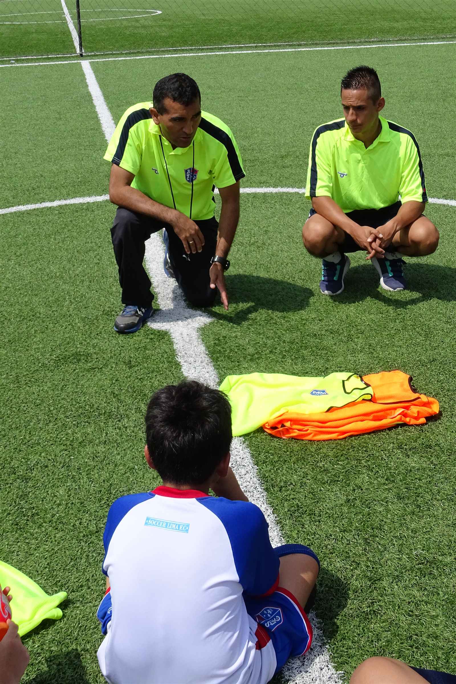 Entrenadores agachados conversando con un alumno, vista desde arriba