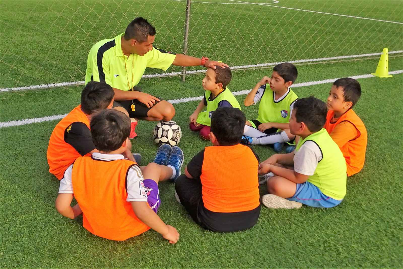 Entrenador con alumnos con petos de colores sentados en círculo en la cancha